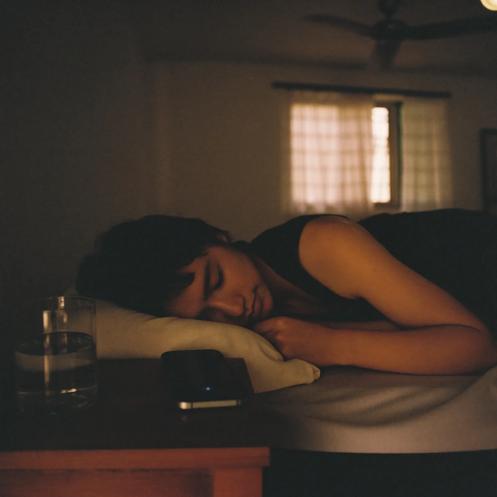 A shop owner asleep at dawn in her room above her shop, her phone dark and face-down on the bedside table.